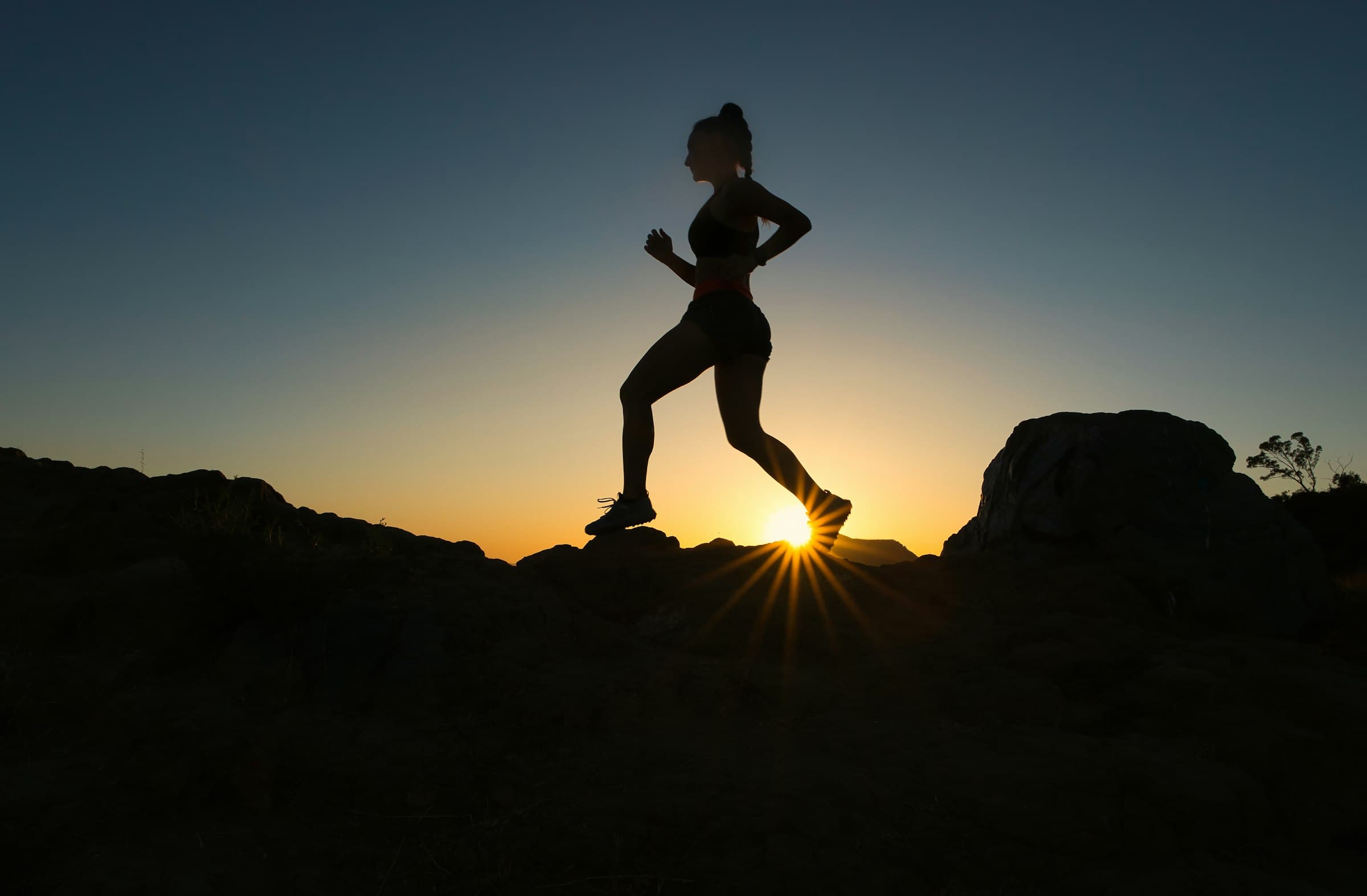 Silhouette of a runner cresting a ridge at sunrise