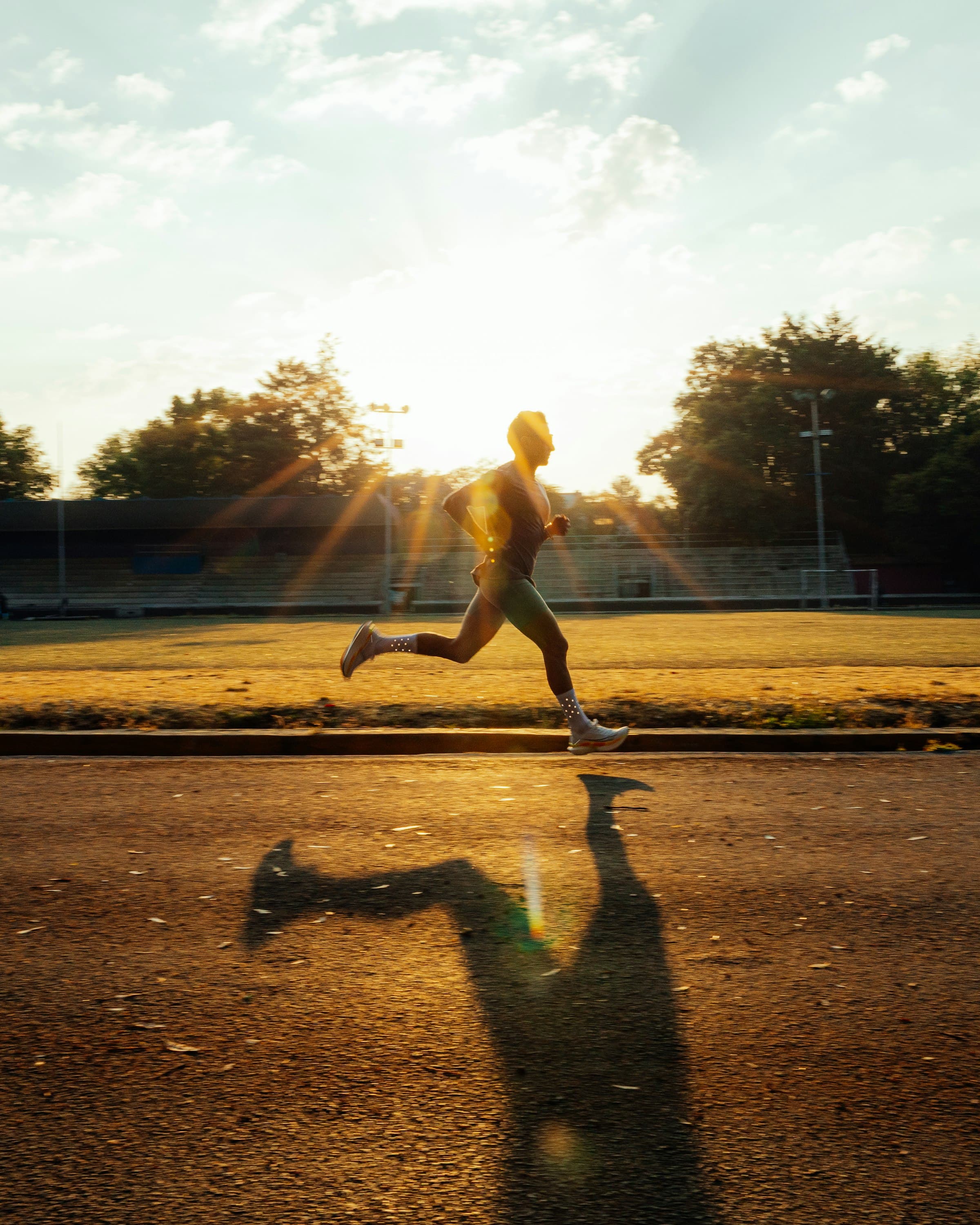 Runner silhouetted against the sun on an empty stadium track