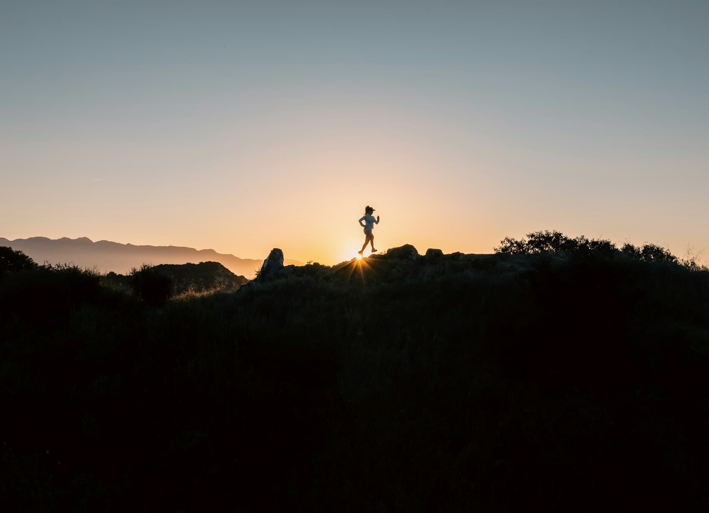 Silhouette of a runner on a hilltop trail at sunset